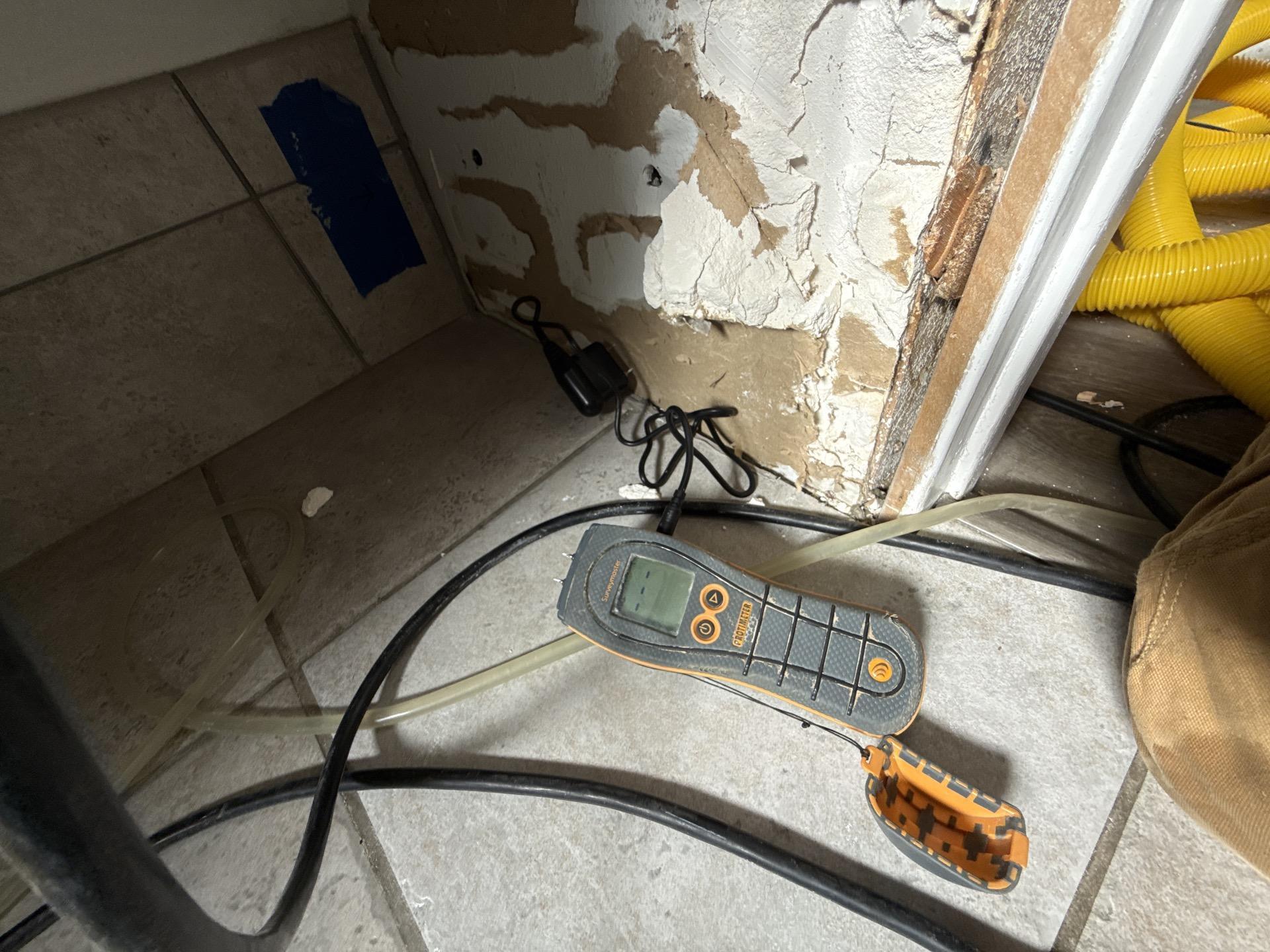Dehumidifier running in bathroom to dry tile floor assembly with moisture migrating down walls