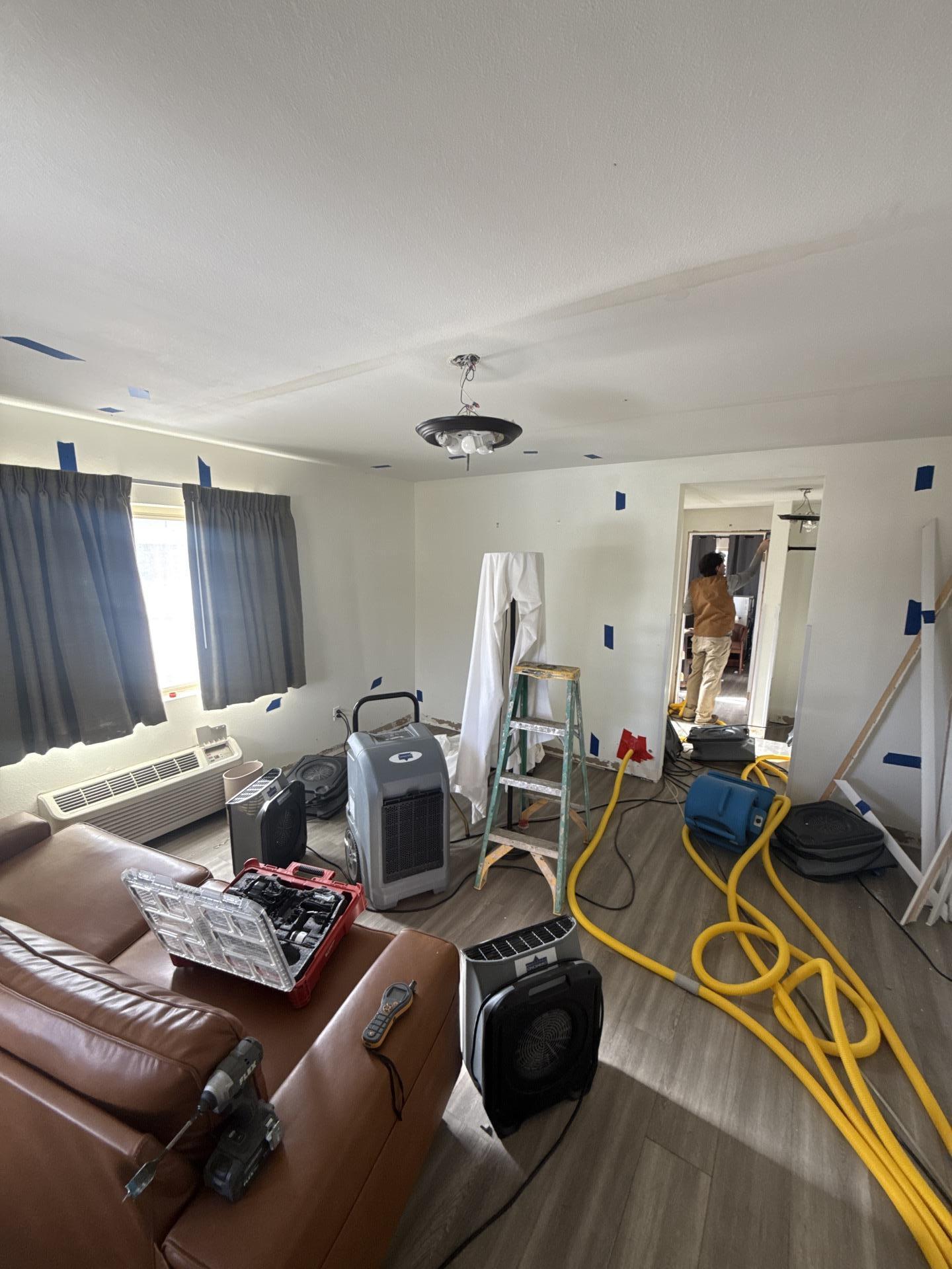 Living room water damage restoration showing air movers and dehumidifier setup on hard flooring