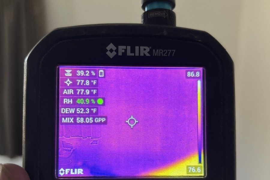 Restoration technician using a thermal imaging camera to detect hidden moisture behind a wall