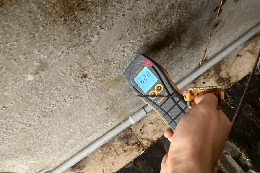 Restoration technician using a moisture meter in a crawl space during a water damage inspection