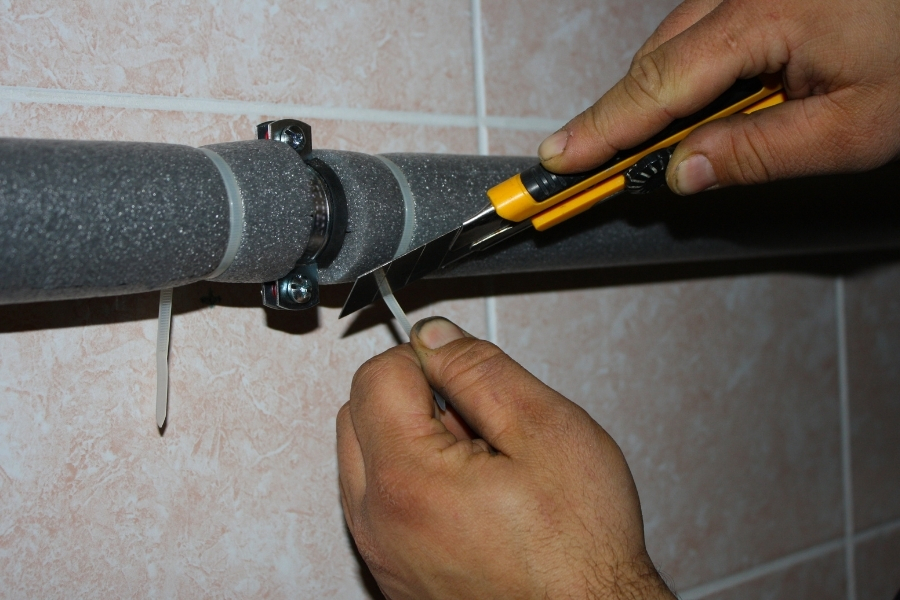 Homeowner sliding foam insulation sleeves onto exposed water pipes to prevent winter freezing