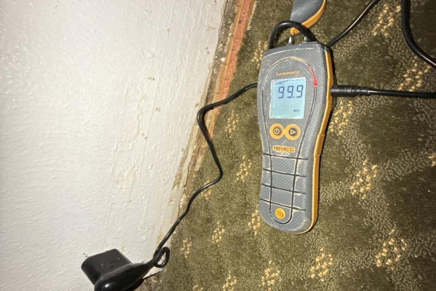 Moisture meter showing a high reading on lower walls during water damage inspection
