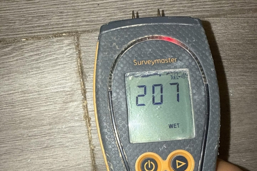 Moisture meter showing hidden water damage under flooring after a frozen pipe leak in a home